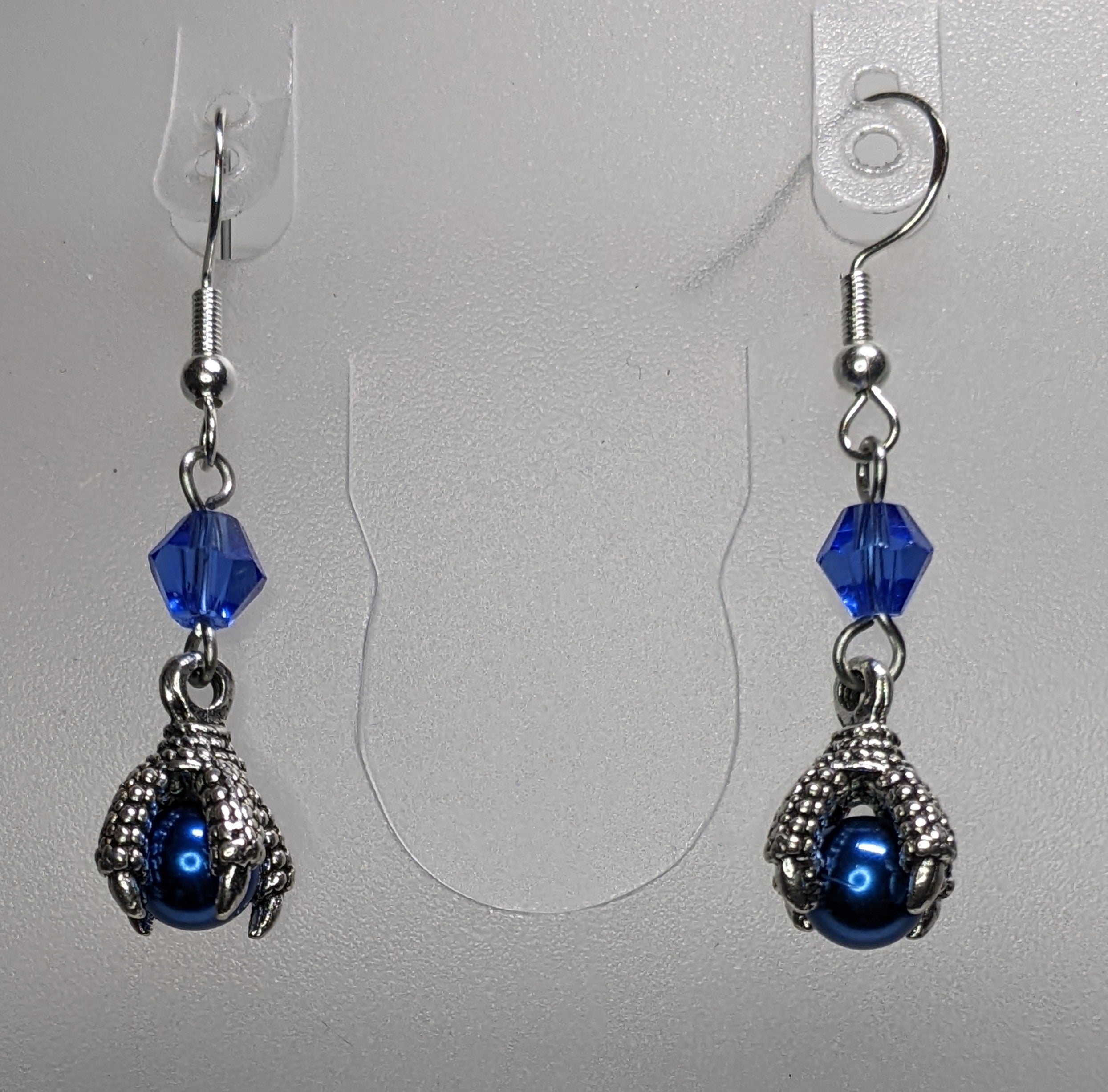 Pair of earrings that have silver dragon claws clutching blue pearls with a faceted bead accents.