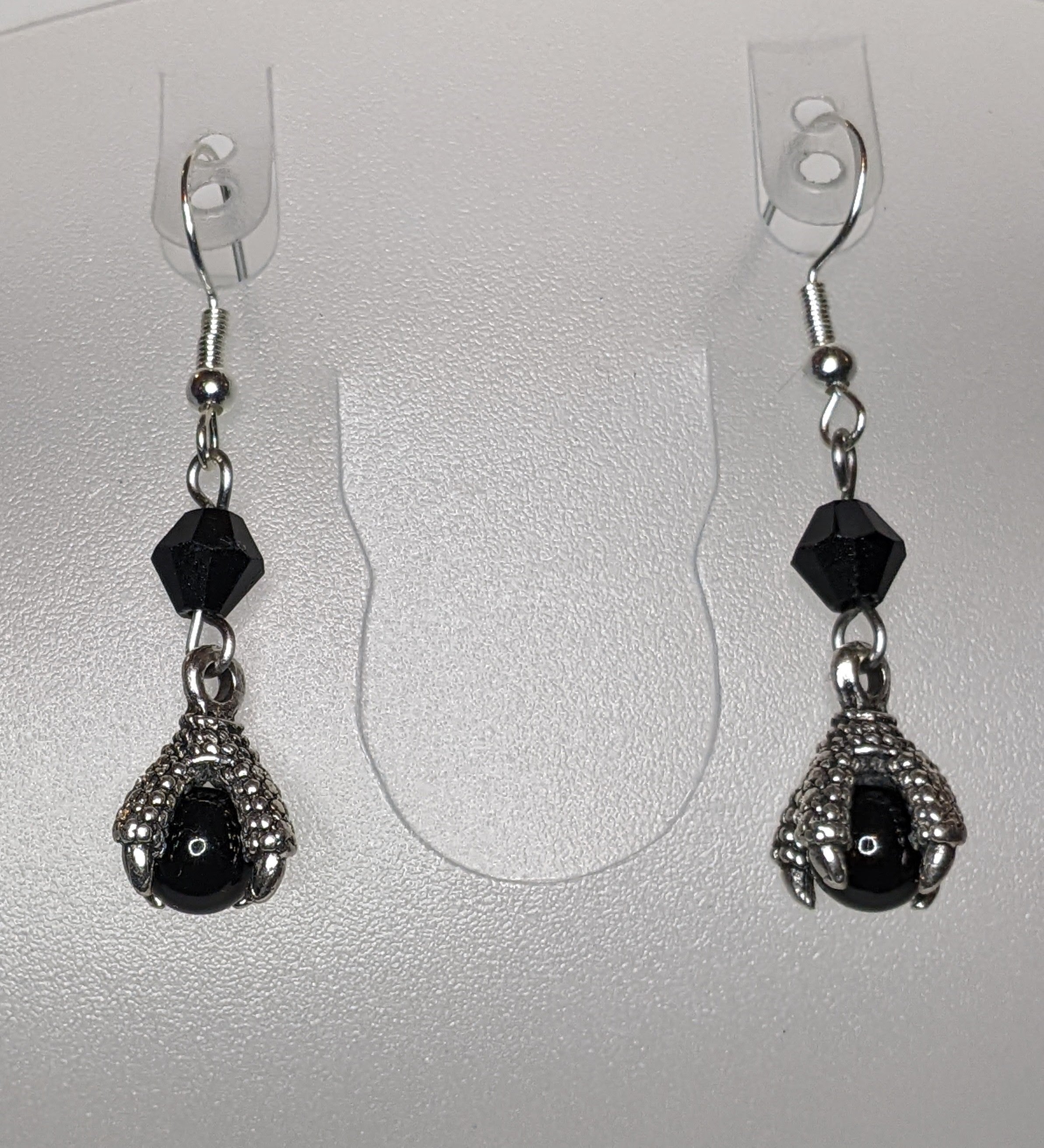 Pair of earrings that have silver dragon claws clutching black pearls with a faceted bead accents.