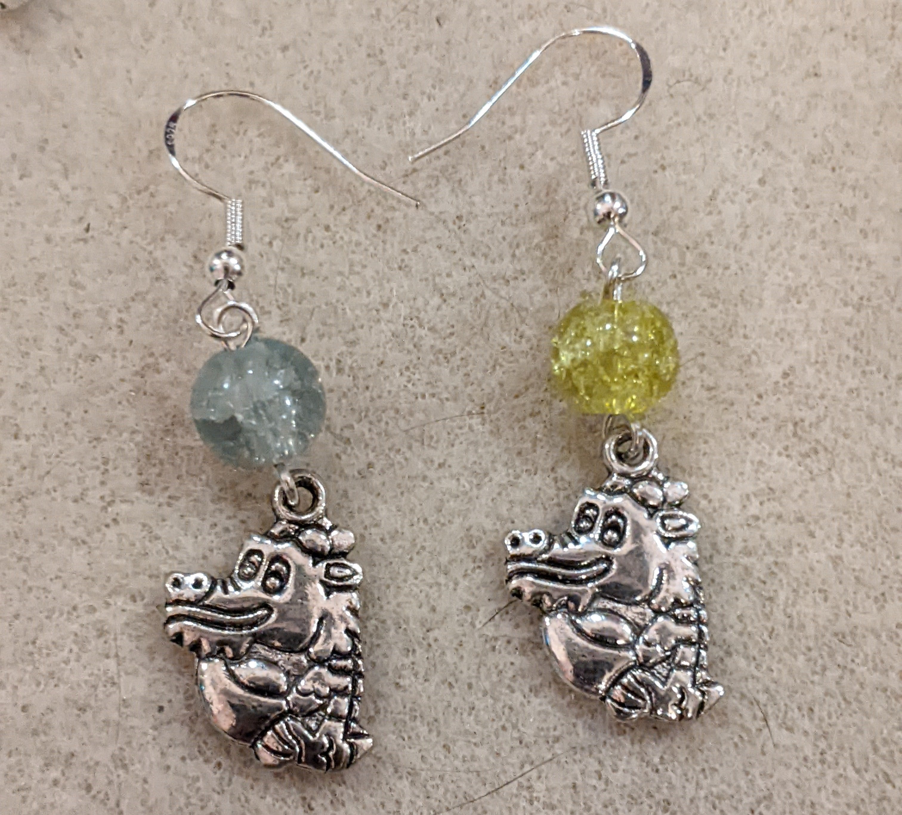 A pair of dangle earrings featuring silver dragon charms and yellow glass bead accents.