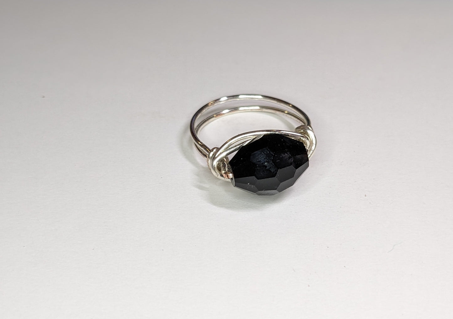 Close up for wire wrapped faceted glass ring on a white background. Ring points slightly to the right.