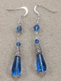Blue Czech pressed glass teardrop dangle earrings with crystal accents on an off-white textured background