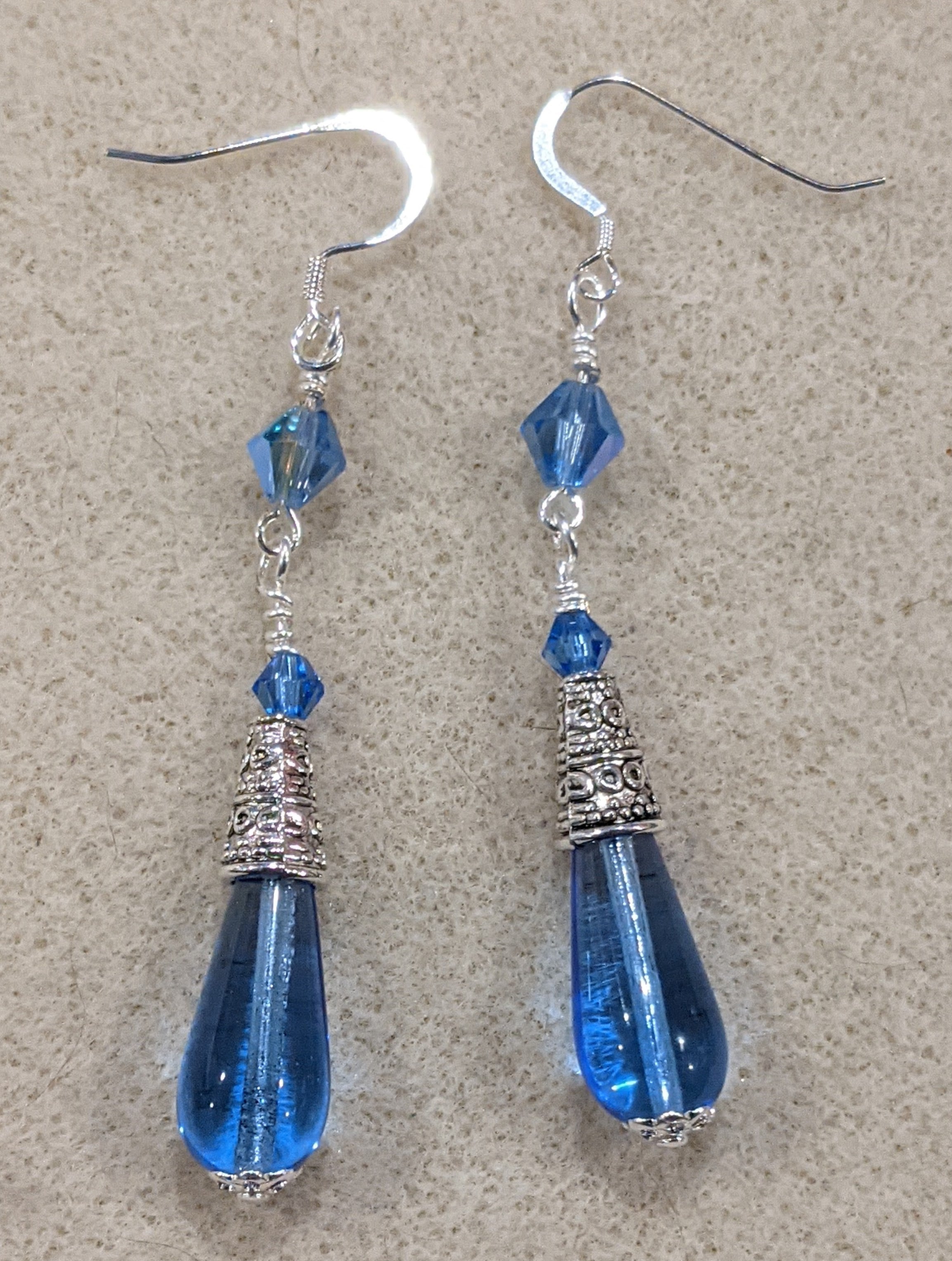 Blue Czech pressed glass teardrop dangle earrings with crystal accents on an off-white textured background