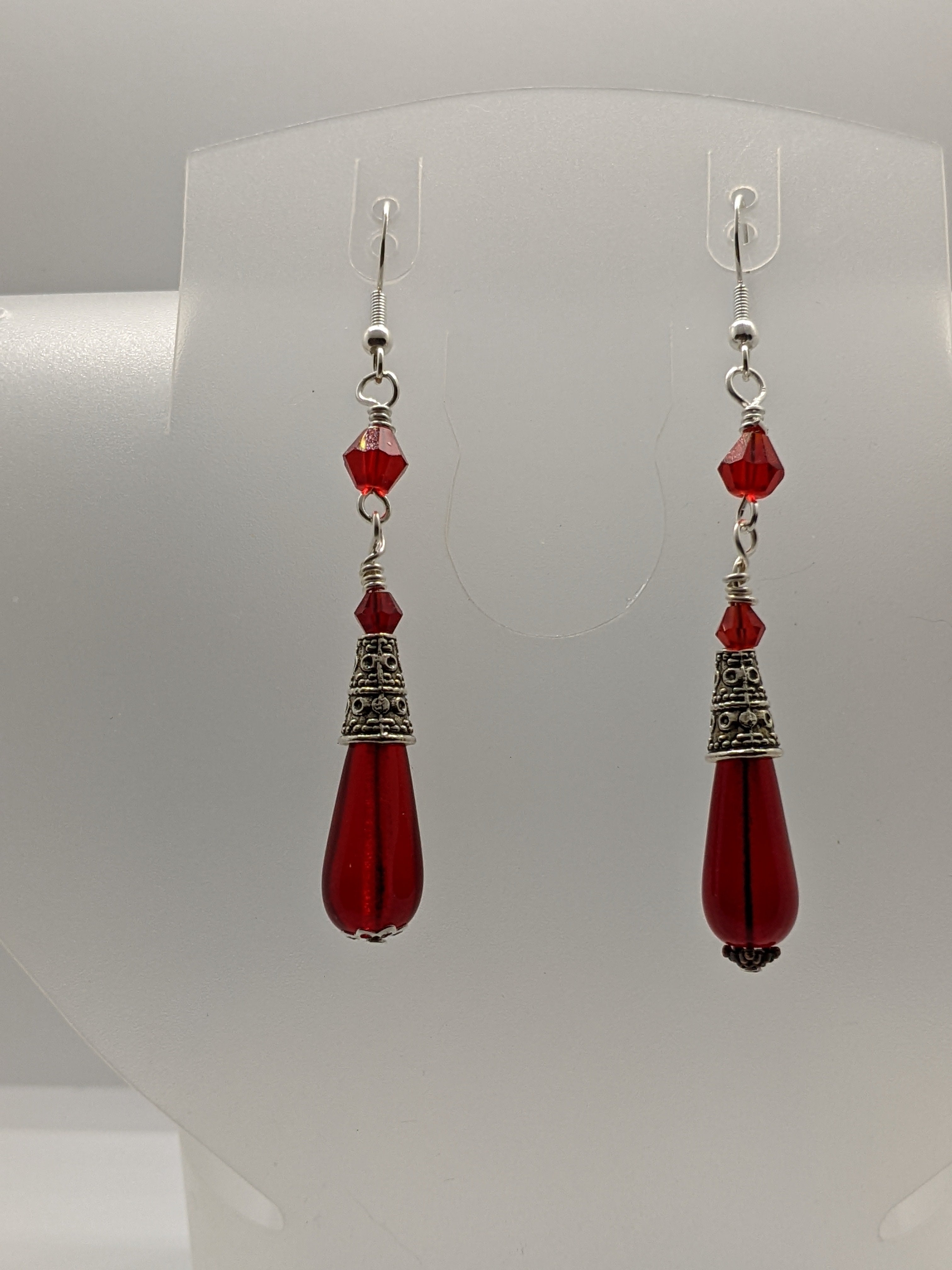 Ruby red Czech glass teardrop earrings with faceted crystal bead accents on an earring display.