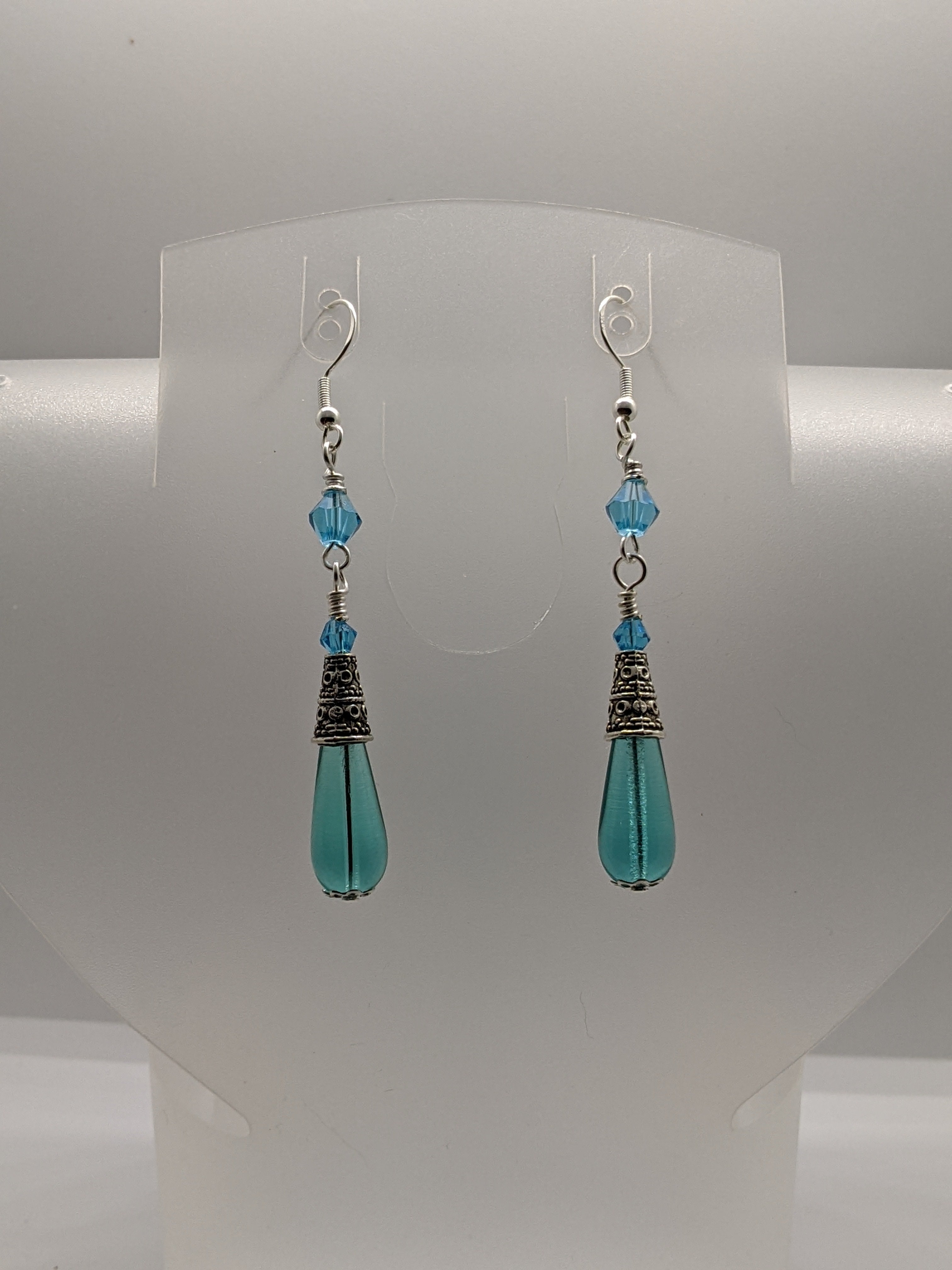 Aqua blue Czech glass teardrop earrings with crystal bead accents on a clear earring display