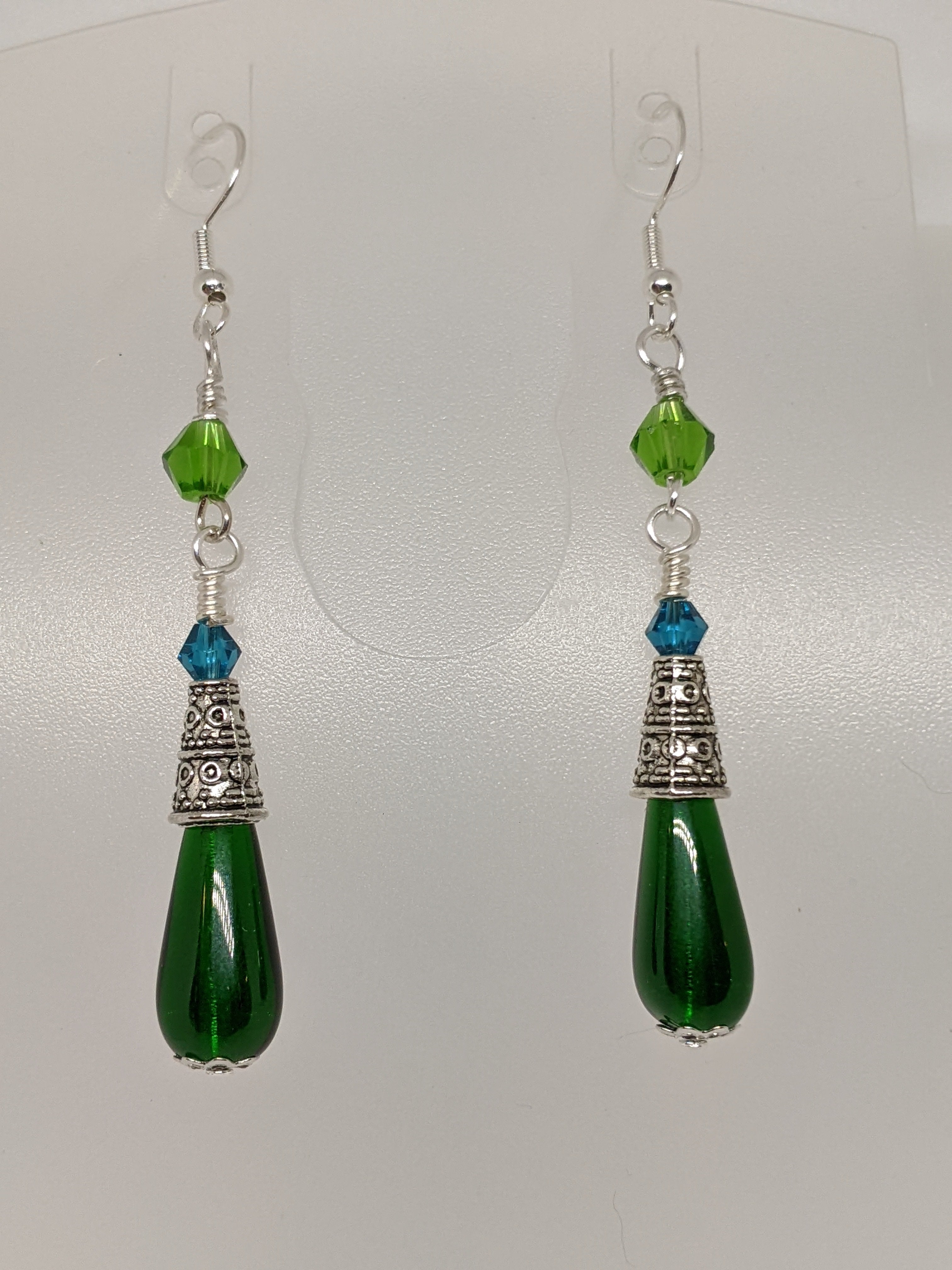 Green Czech pressed glass teardrop dangle earrings with crystal accents on an earring display