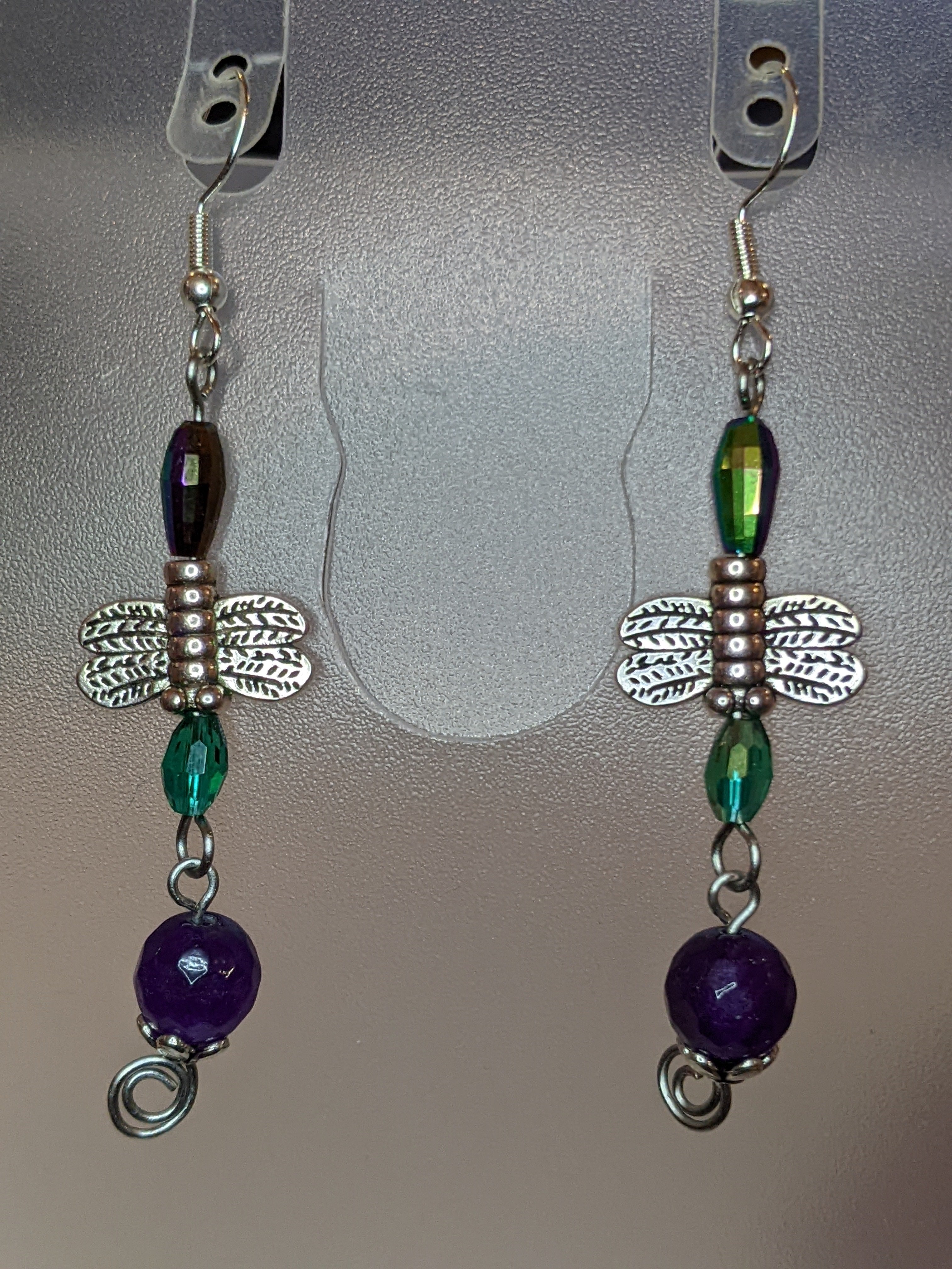A pair of beaded dangle earrings featuring purple and green beads with silver-colored dragonfly charms.