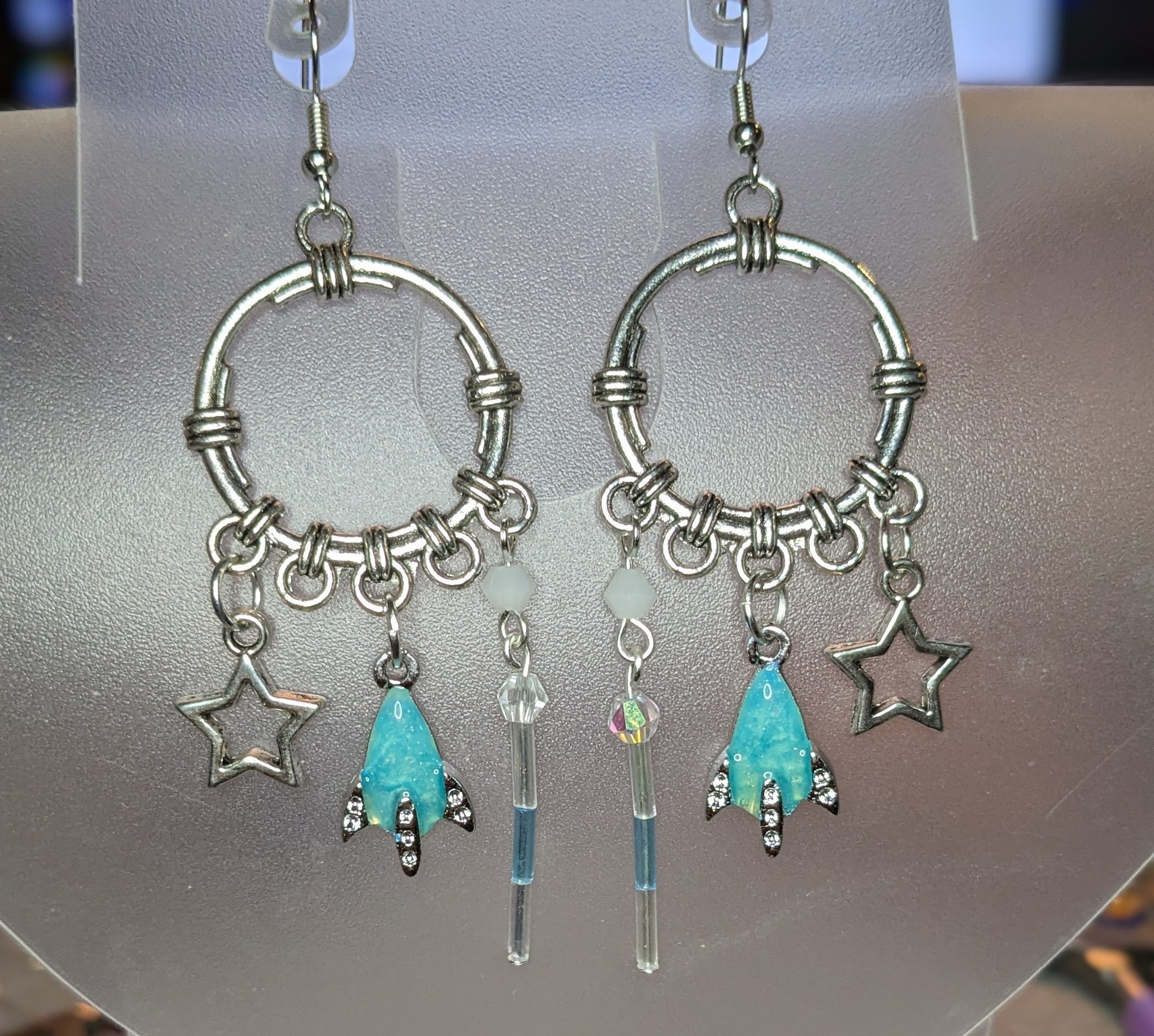 Pair of silver hoop earrings with star and turquoise charm on a gray background