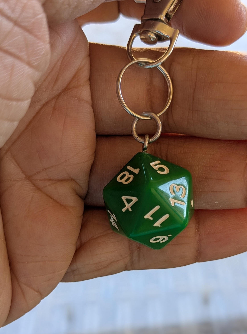 Green D20 keychain held in a person's fingers