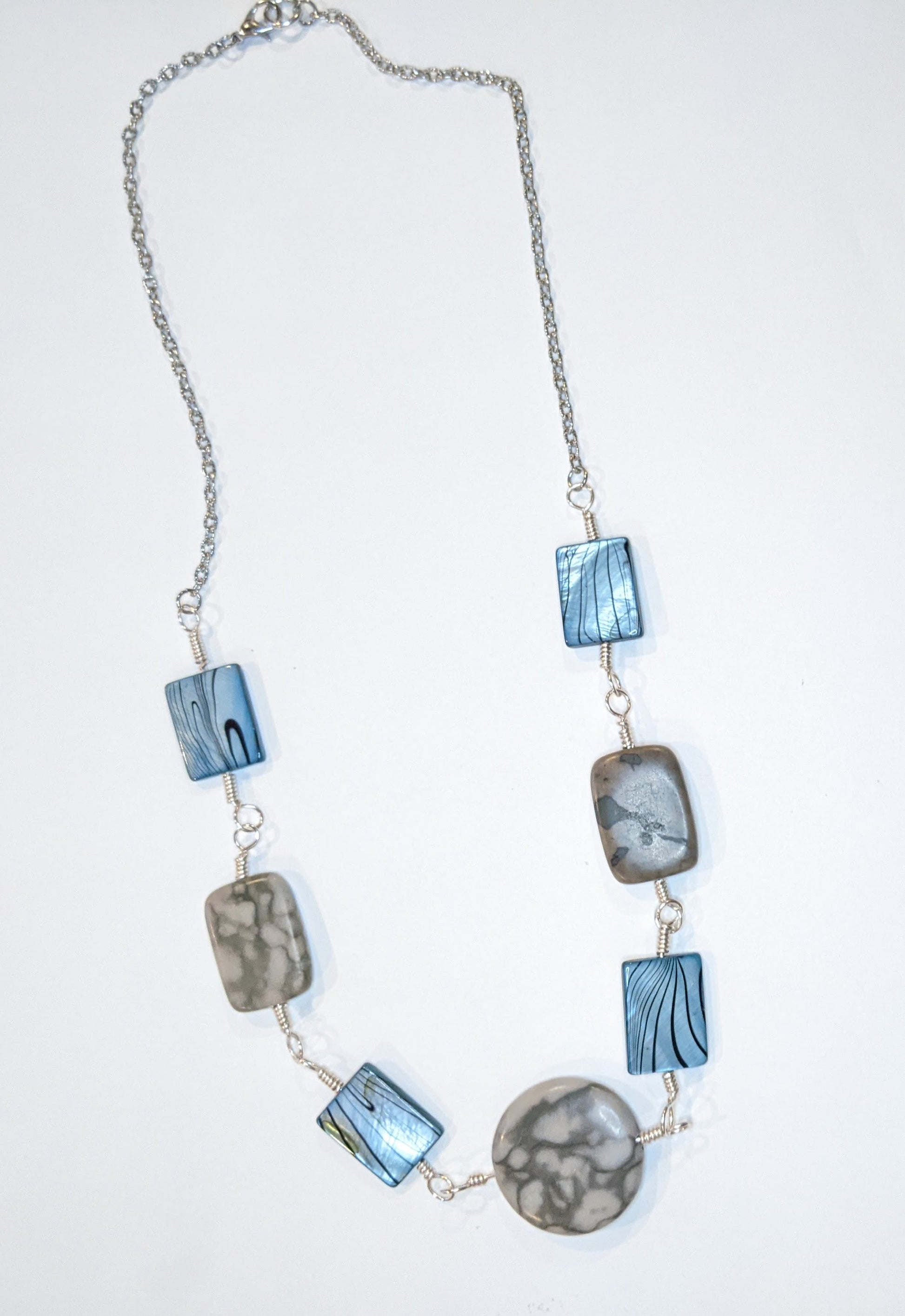 Linked component necklace on a white background. The wire wrapped links are of grey marble canyon and dyed shell alternating. The center is a round marble canyon bead and the other beads are rectangular. 