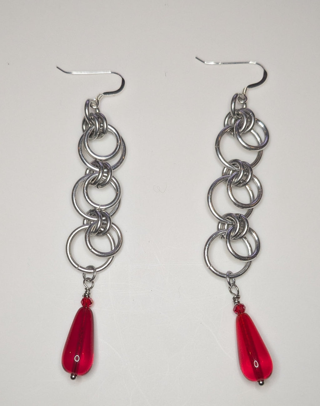 Silver chain earrings with red teardrop charms on a white background