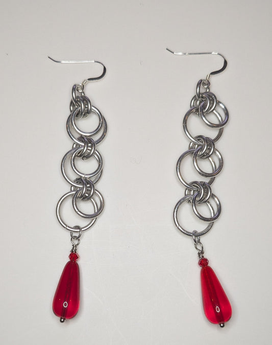 Silver chain earrings with red teardrop charms on a white background