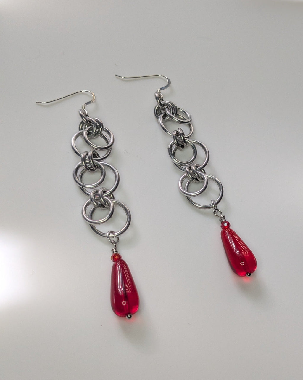 Silver chain earrings with red teardrop charms on a light gray background