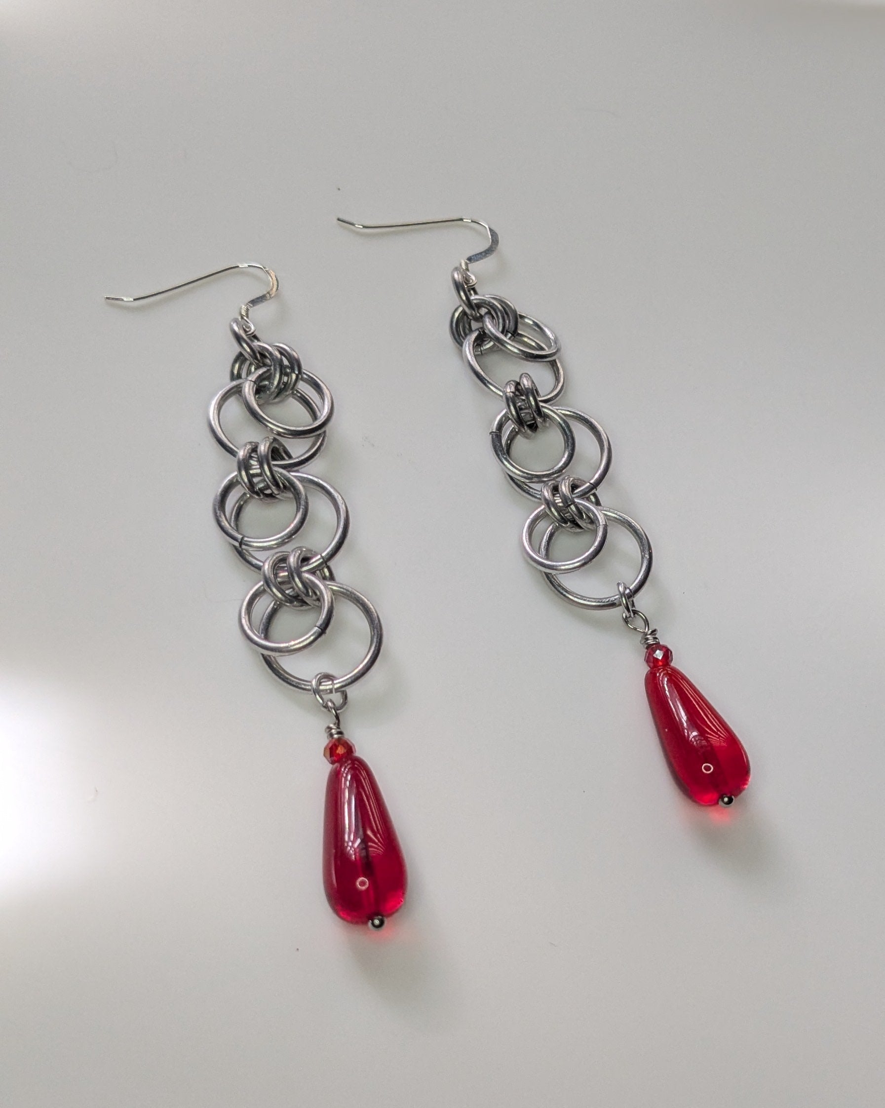 Silver chain earrings with red teardrop charms on a light gray background