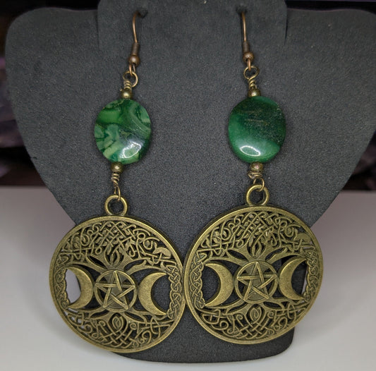Pair of bronze filigree detailed earrings with green beads on a gray stand.