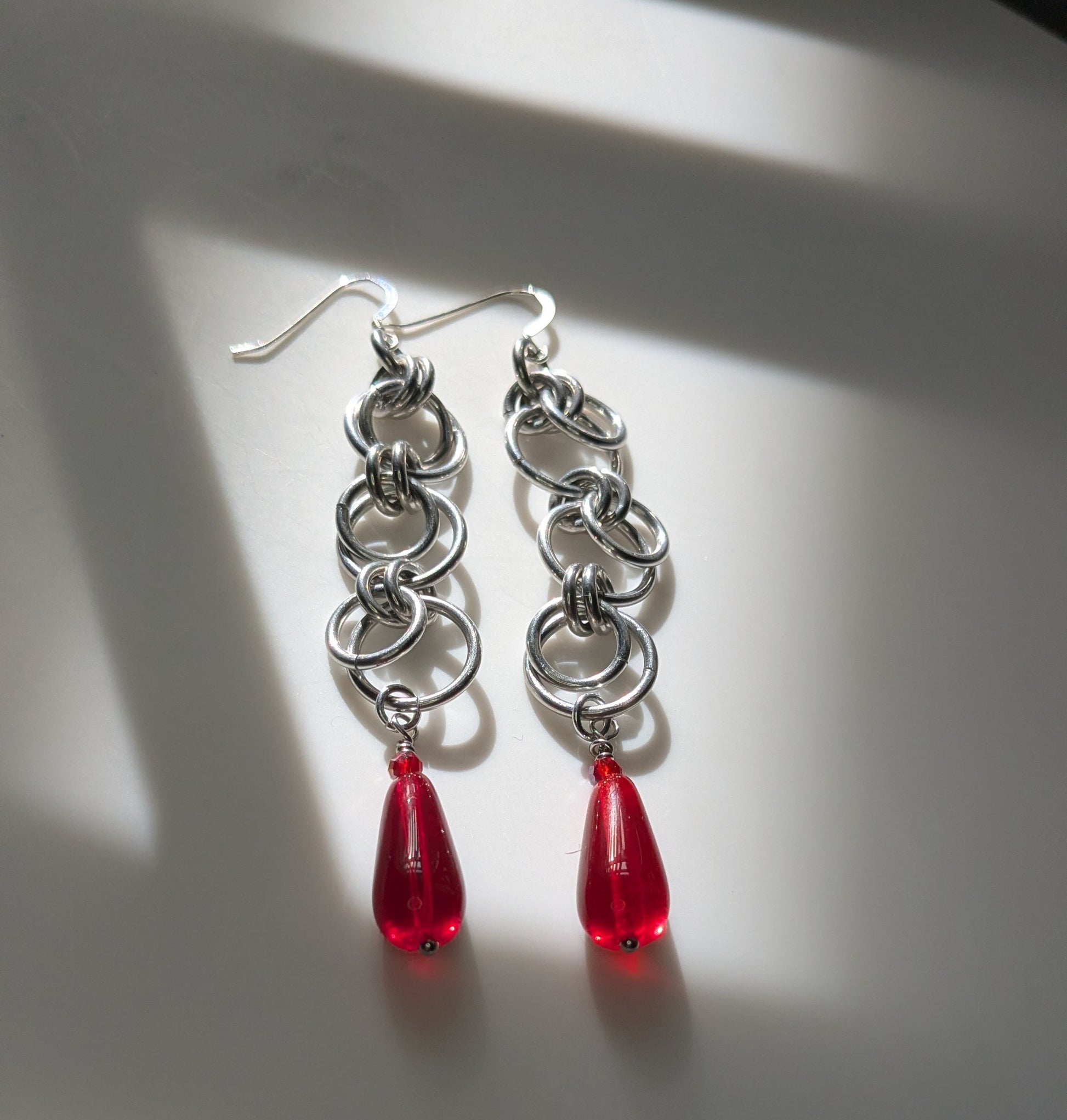 Silver chain earrings with red teardrop beads on a light background